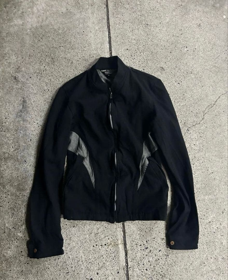 Front view flat-lay of a black COMME des GARCONS Homme Plus men's cotton jacket on a concrete floor.